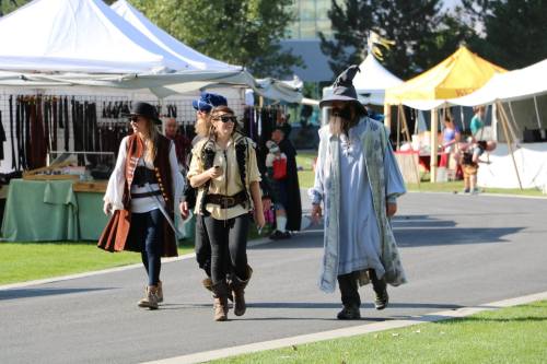 Four people in costumes walk through a festival, with tents and greenery in the background.