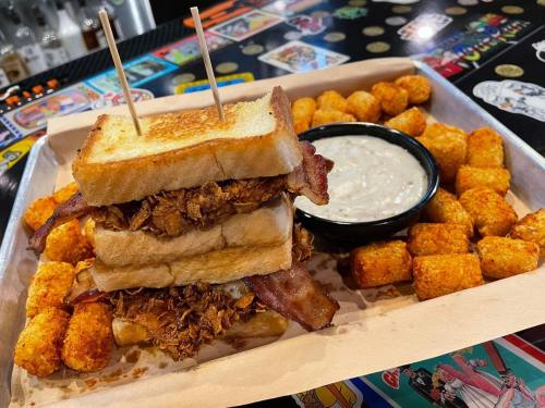A towering sandwich with crispy chicken and bacon, served with tater tots and a side of dipping sauce.