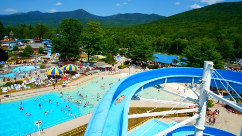 Aerial view of a vibrant water park with slides, pools, and visitors enjoying a sunny day surrounded by mountains.