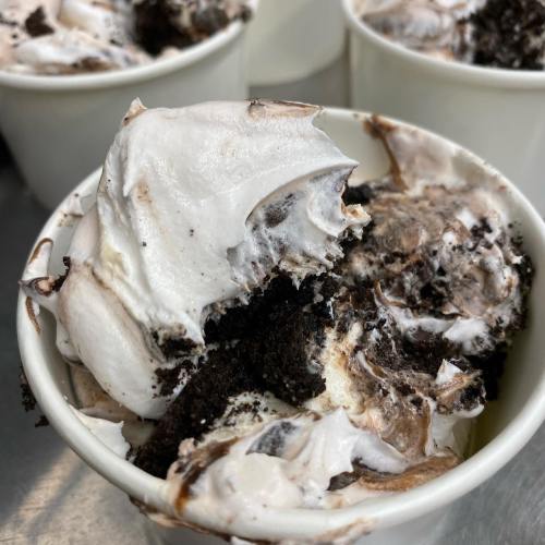Close-up of a cup filled with creamy dessert, featuring swirls of whipped cream and crushed chocolate cookies.