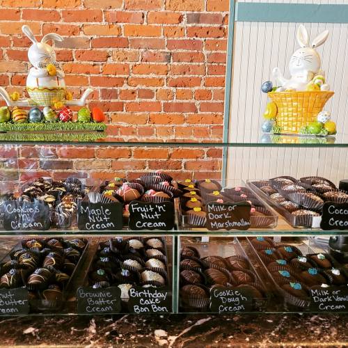 A display case filled with assorted chocolates and candies, with a decorative Easter-themed background.