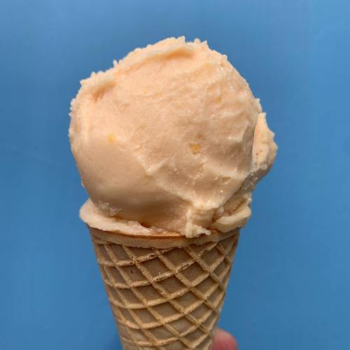 A close-up of a peach-flavored ice cream scoop in a waffle cone against a blue background.