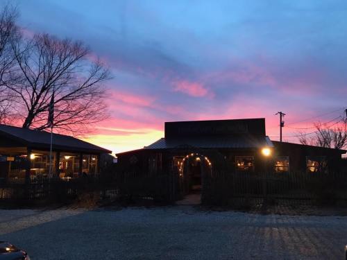 A rustic building illuminated at dusk, with a vibrant pink and purple sunset in the background.