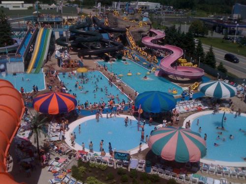 Aerial view of a busy water park with pools, water slides, and colorful umbrellas on a sunny day.