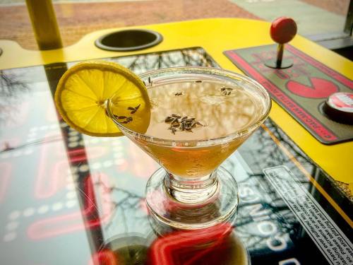 A cocktail with a lemon slice and herbs sits on a colorful arcade game table.