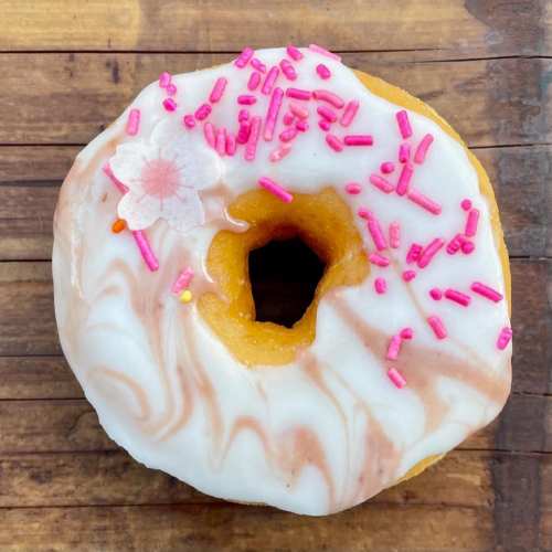 A glazed donut topped with pink sprinkles and a flower decoration on a wooden surface.
