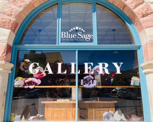 Window display of Blue Sage Center for the Arts featuring the word "GALLERY" and decorative paper flowers.