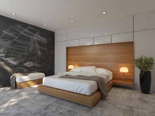 Modern bedroom with a wooden bed, bedside lamps, a single bed, and a chalkboard wall featuring a ship drawing.