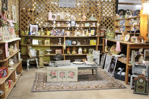 A cozy vintage shop filled with shelves of decorative items, antiques, and a central table on a patterned rug.