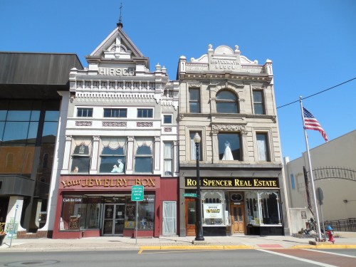 Historic buildings with ornate facades, featuring a jewelry store and real estate office, under a clear blue sky.