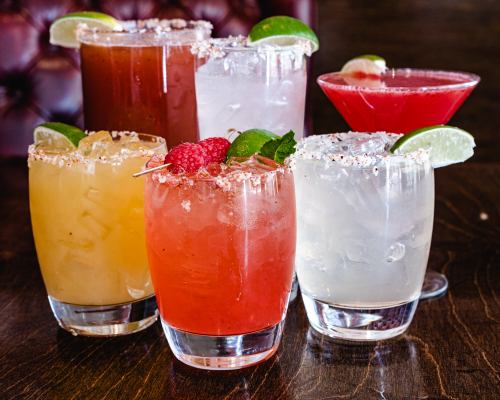 A colorful assortment of six cocktails with garnishes, served in glasses on a wooden table.