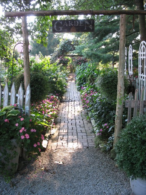 A serene garden path lined with flowers and greenery, leading to a wooden sign that reads "Garden."