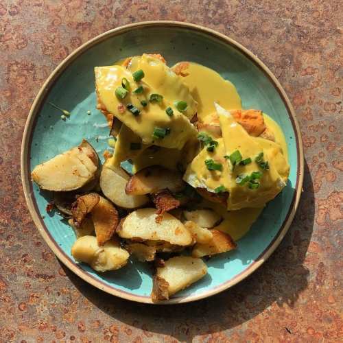 A plate of golden-brown roasted potatoes and two pieces of fish topped with creamy sauce and green onions.
