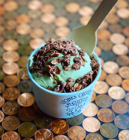 A cup of mint ice cream topped with chocolate granola, placed on a surface covered with shiny pennies.