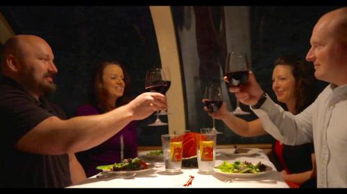 A group of four friends toasting with glasses of red wine at a dinner table, enjoying a meal together.