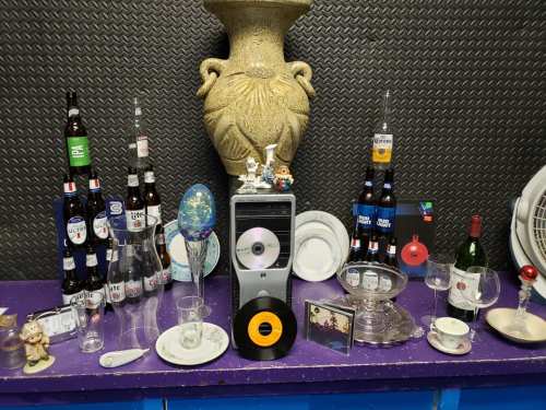 A colorful display of bottles, glasses, and decorative items arranged on a purple surface with a large vase in the background.