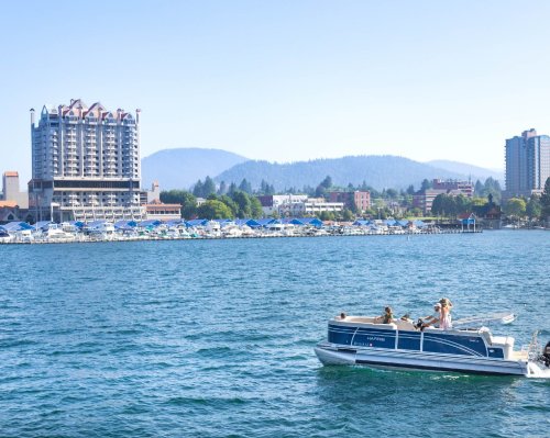 A boat with people cruises on a lake near a city skyline and mountains under a clear blue sky.