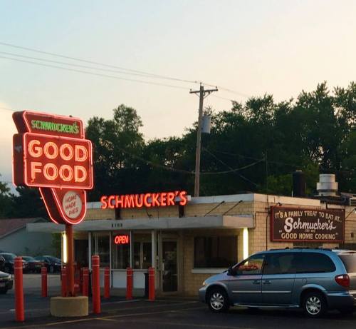 A diner named Schmucker's with a neon sign reading "Good Food" and "Open," surrounded by trees and a parking lot.