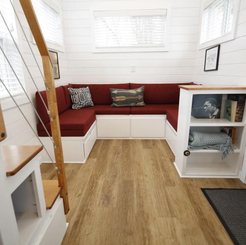 Cozy interior of a tiny home featuring a red corner seating area, wooden stairs, and light wood flooring.