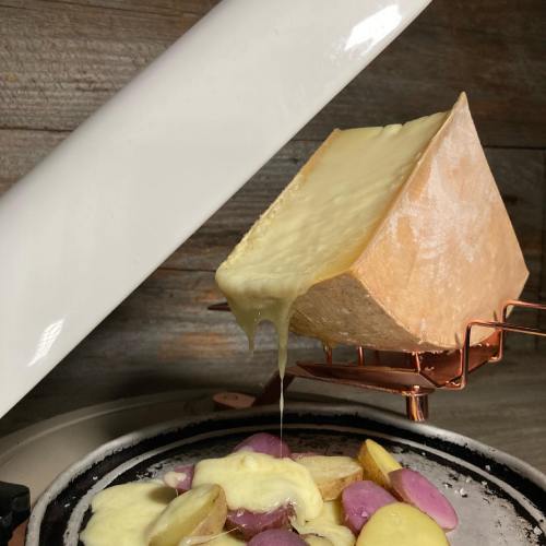 Melted cheese pouring over colorful sliced potatoes on a grill, with a rustic wooden background.