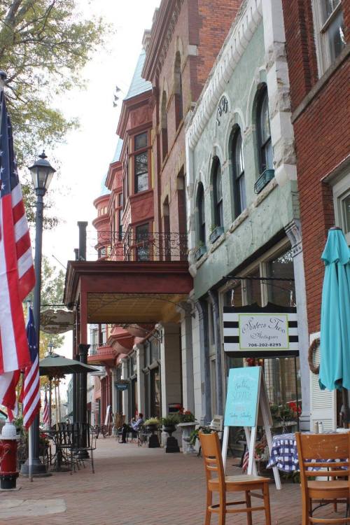 A charming street lined with historic buildings, outdoor seating, and an American flag, creating a quaint atmosphere.