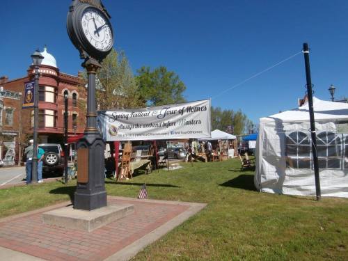 A clock tower stands near a banner for a spring festival, with tents and displays set up in a grassy area.