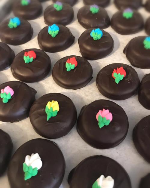A tray of chocolate-covered cookies, each topped with colorful flower decorations.