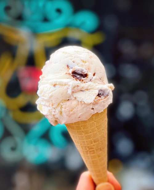 A hand holding a cone of ice cream with chocolate chunks against a colorful, blurred background.