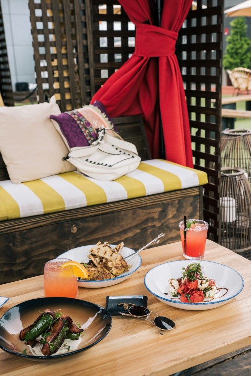 A cozy outdoor dining setup featuring colorful dishes, drinks, and a stylish bag on a wooden table.