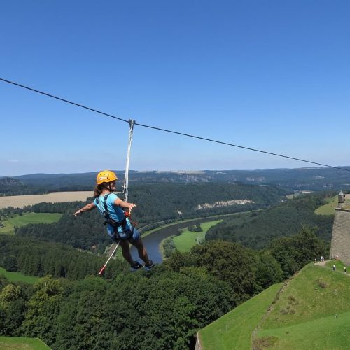A person zip-lining over a lush green valley with a clear blue sky in the background.