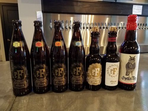 A lineup of various beer bottles on a bar counter, featuring different labels and designs.