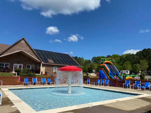 A pool with a fountain in the center, surrounded by lounge chairs, with a colorful inflatable slide in the background.
