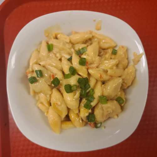 A bowl of creamy pasta with small shells, topped with chopped green onions, served on a red tray.