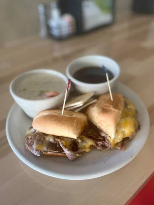 A plate with two cheesy sandwiches, a bowl of soup, and a small dish of sauce, garnished with toothpicks.