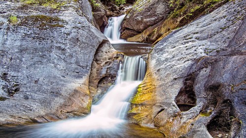 A serene waterfall cascading over smooth, rocky terrain surrounded by lush greenery.