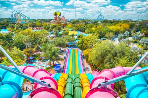 A vibrant water park view featuring colorful slides, lush greenery, and attractions under a bright blue sky.