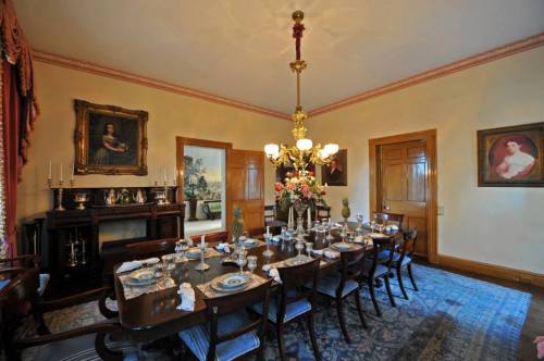 Elegant dining room with a long table set for a meal, featuring floral arrangements and classic artwork on the walls.