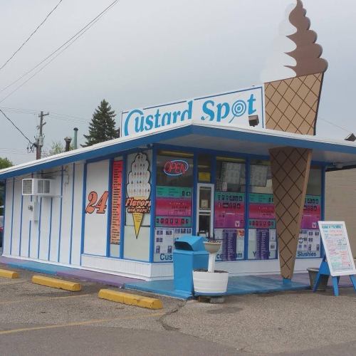 A colorful ice cream shop called "Custard Spot" with a large ice cream cone sign and an open sign.