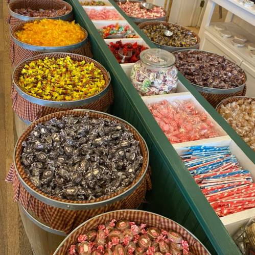 A colorful display of various candies in wooden bins, featuring wrapped sweets and lollipops.