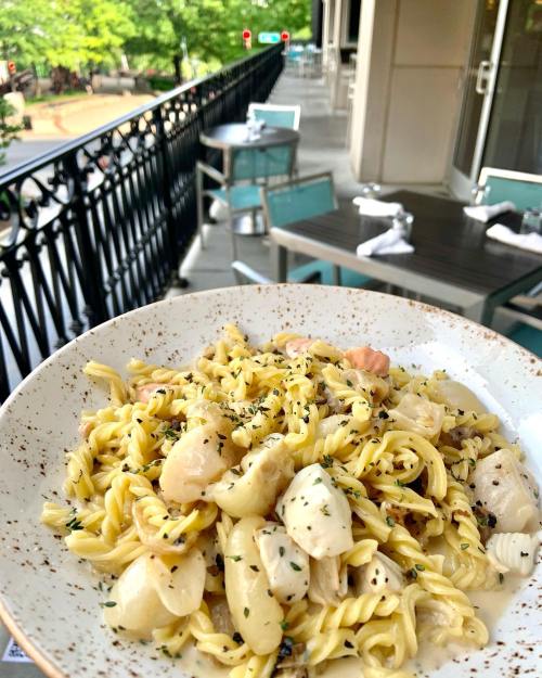 A plate of pasta with chicken and herbs, set on a table with a view of an outdoor dining area.