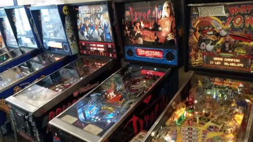 A collection of vintage pinball machines in a game arcade, featuring colorful designs and illuminated playfields.