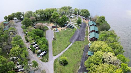 Aerial view of a lakeside campground with cabins, RVs, and green trees surrounding the water.