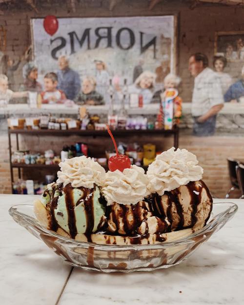 A delicious ice cream sundae with three scoops, whipped cream, chocolate sauce, and a cherry, set against a vintage backdrop.