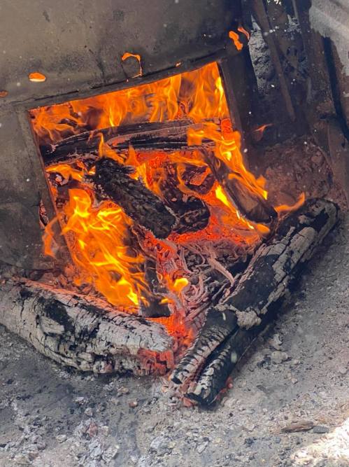 A close-up of a fire burning logs in a metal container, with bright flames and glowing embers.