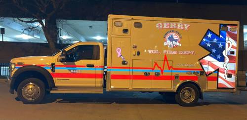 A fire department ambulance with patriotic designs and a pink ribbon, parked in a well-lit area at night.