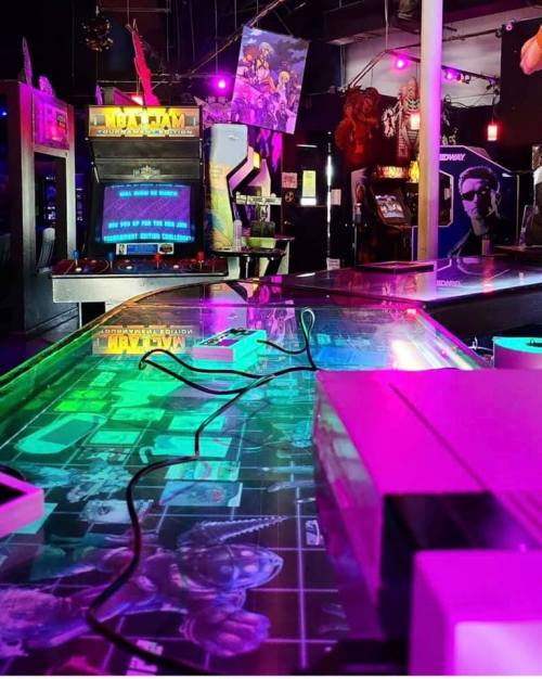 A vibrant arcade filled with retro games, neon lights, and colorful decor, showcasing classic arcade machines.