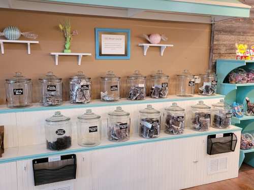 A display of glass jars filled with various candies on a shelf, with a sign indicating the price per pound.