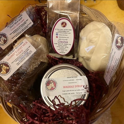 A gift basket filled with goat milk fudge, syrup, and assorted treats from a farm, arranged with decorative filler.