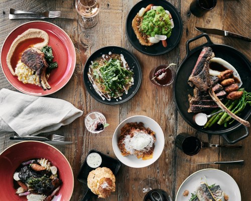 A table spread with various gourmet dishes, including meats, vegetables, and desserts, set on rustic wooden surfaces.