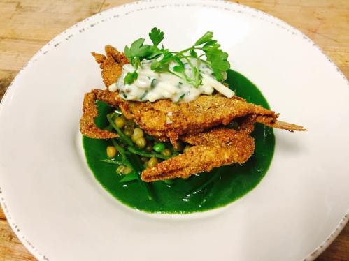 A plate of fried soft-shell crabs on a bed of green sauce, garnished with herbs and served with peas.